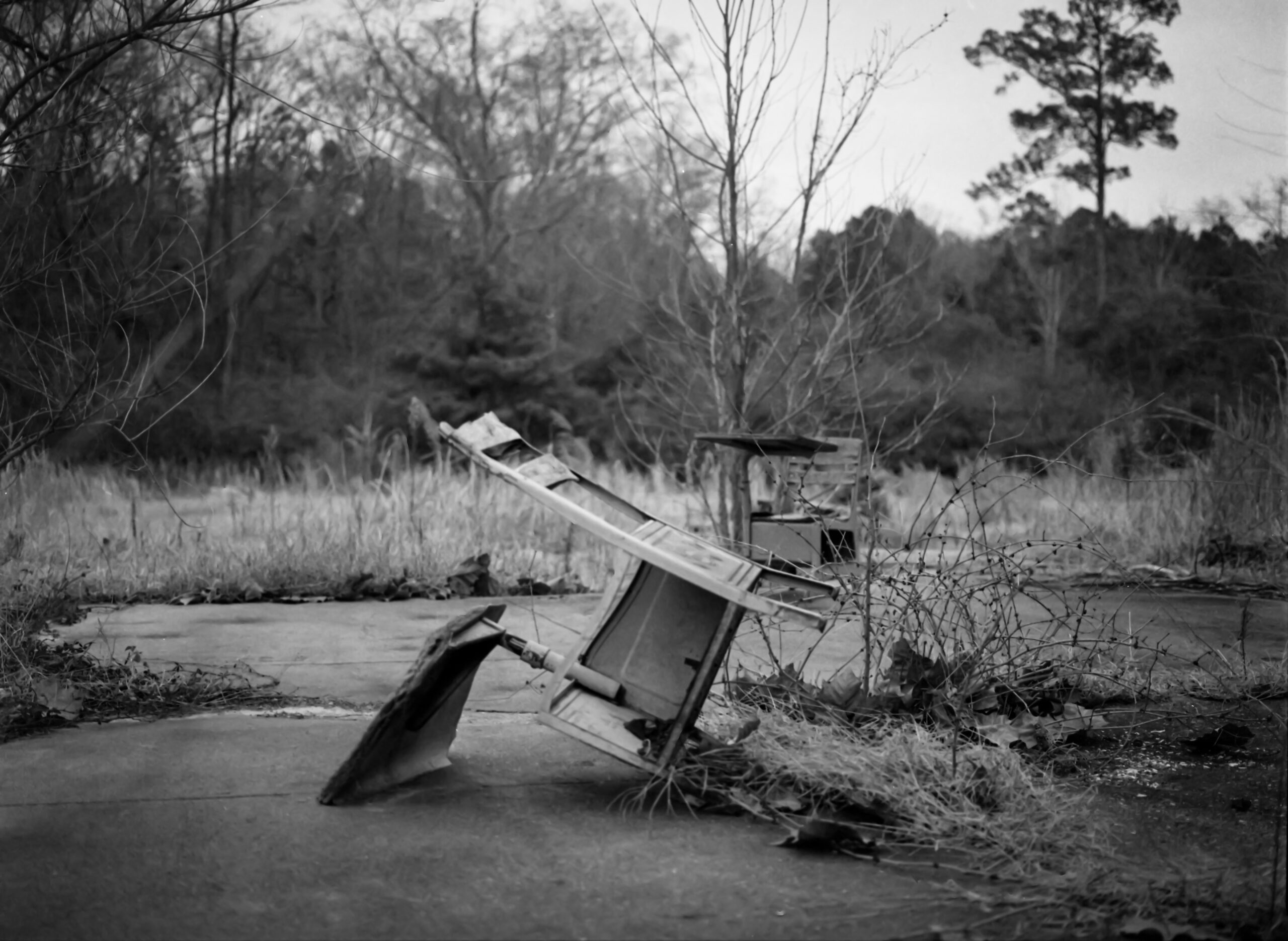 Black and White photograph of an abandoned school desk overturned on an empty concrete pad.